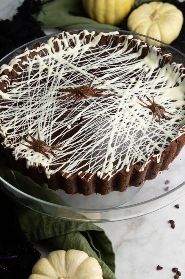 A chocolate tart with white chocolate stenciled like spiderwebs with chocolate spiders. 