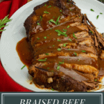 A braised beef brisket sliced and arranged on a white platter with red wine gravy