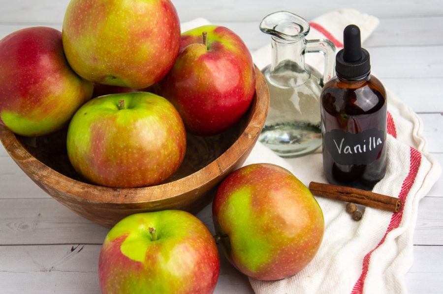 a wooden bowl of apples on a white and red towel with vanilla, water, and cinnamon