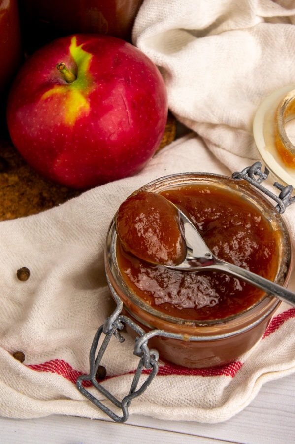 a jar of apple butter with a spoon resting across it on a white towel with a red stripe