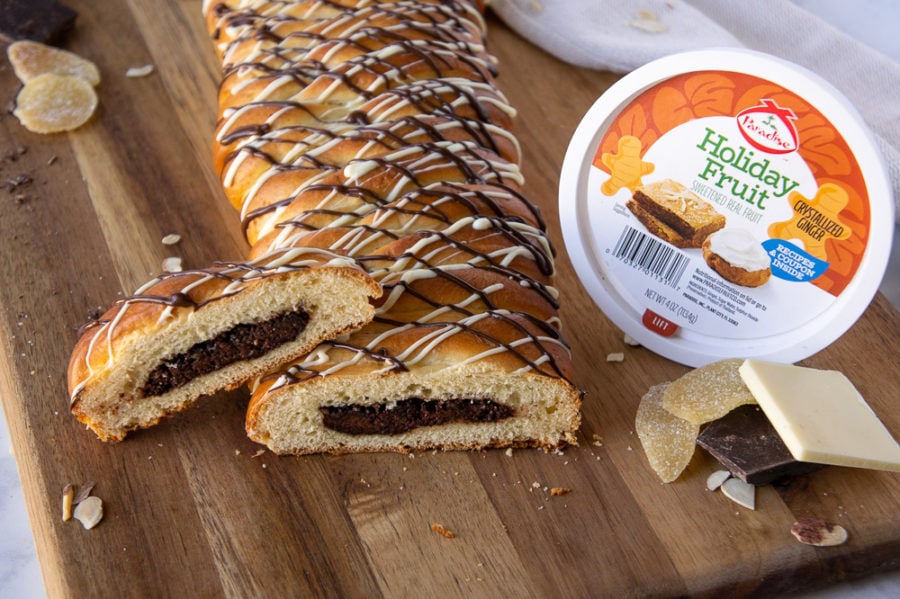 Chocolate filled bread with the end sliced open to display the chocolate filling on a wooden cutting board beside a container of Paradise candied ginger.