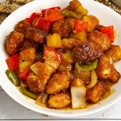 a large white bowl of sweet and sour chicken with pineapple and peppers