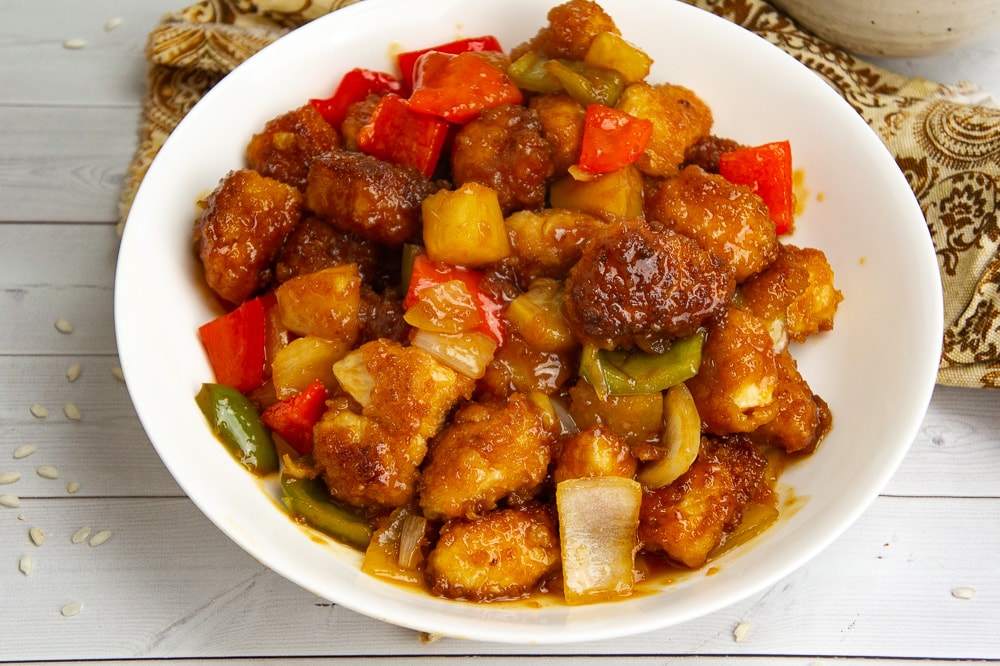 a large white bowl of sweet and sour chicken with pineapple and peppers
