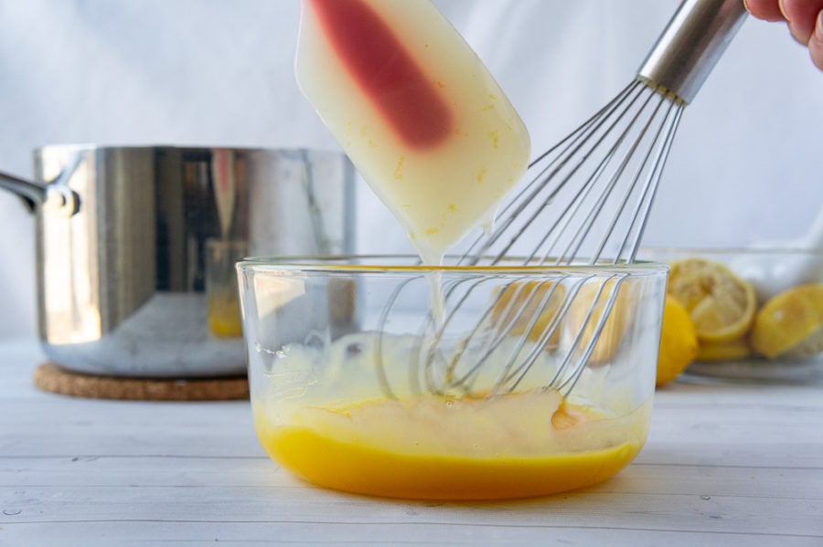 thickened lemon filling being whisked into egg yolks in a small bowl