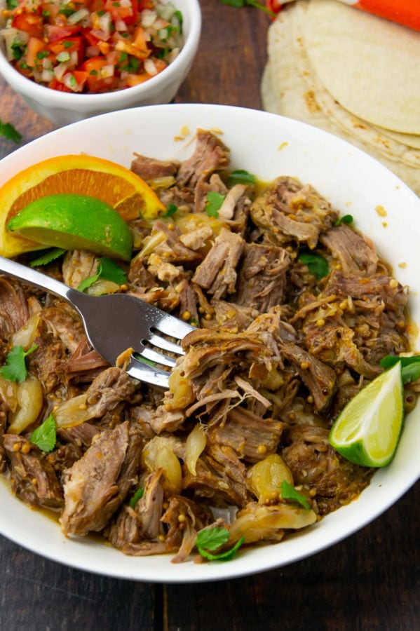 a white bowl with pulled pork topped by cilantro and citrus wedges