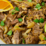 a bowl of shredded pork with cilantro and an orange wedge