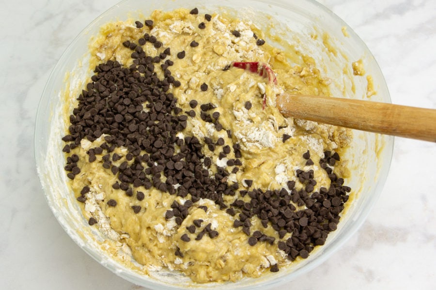 a bowl of banana muffin batter with chocolate chips being added