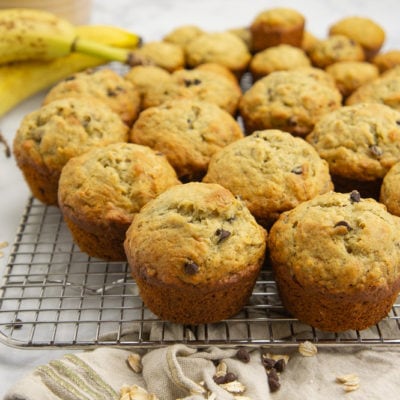 a cooling rack with muffins stacked on it beside a banana and brown linen towel