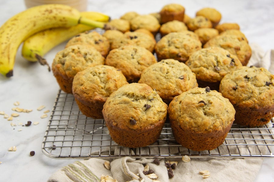 a cooling rack with muffins stacked on it beside a banana and brown linen towel