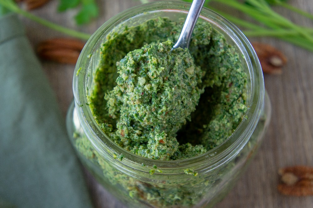 a jar of carrot top pesto with a spoon in it