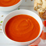 two bowls of carrot tomato soup with bread