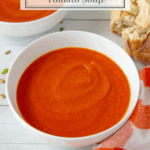 a bowl of tomato carrot soup next to an orange checked towel