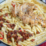 a wide pan of creamy chicken pasta with bacon and bell peppers