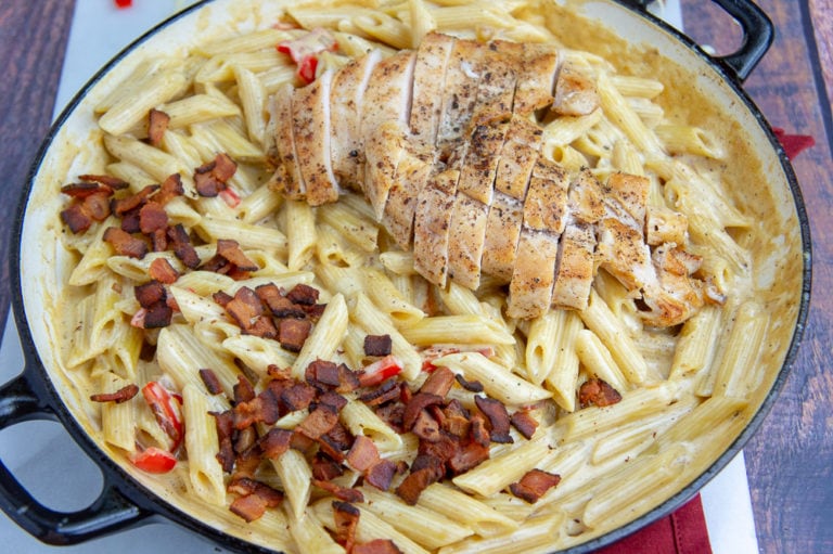 a wide pan of creamy chicken pasta with bacon and bell peppers