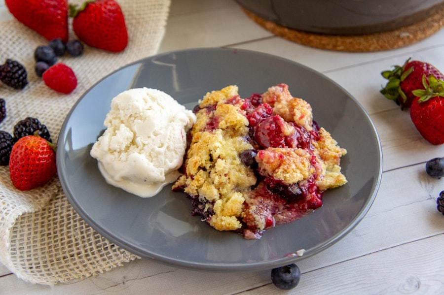a scoop of mixed berry cobbler with a scoop of vanilla ice cream on a gray plate