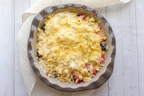 a gray pie plate with mixed berries and cobbler topping with melted butter poured over the top