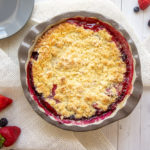 a mixed berry cobbler on a white table with berries around it