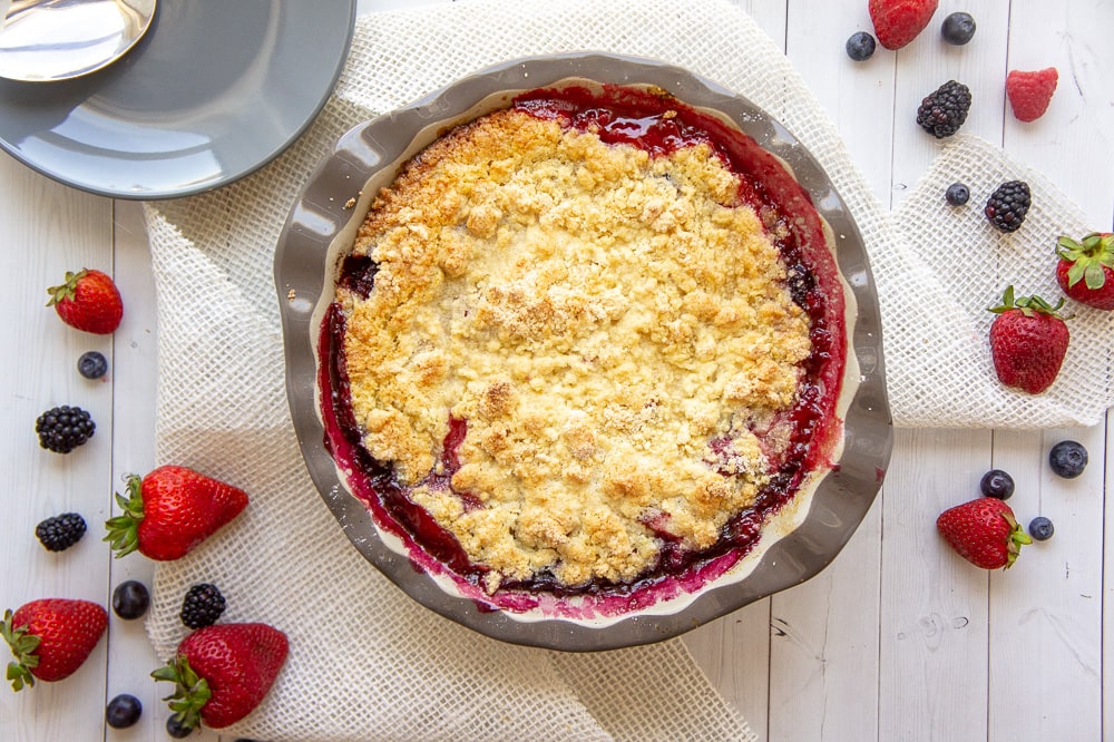 a mixed berry cobbler on a white table with berries around it