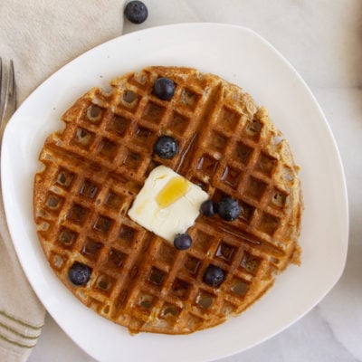 a whole wheat waffle on a white plate next to a fork