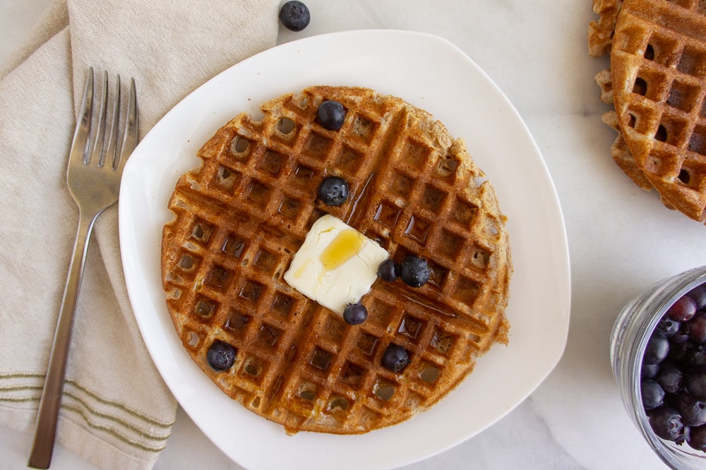 a whole wheat waffle on a white plate next to a fork