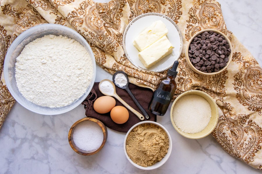 bowls of flour, sugars, chocolate chips, butter and salt with eggs and vanilla