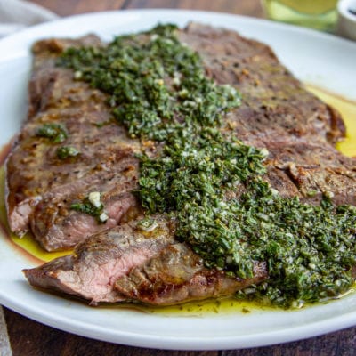 flank steak with chimichurri on a white plate
