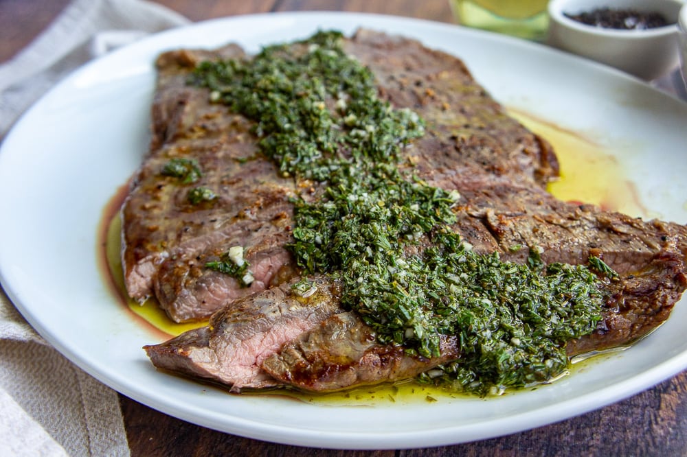 flank steak with chimichurri on a white plate
