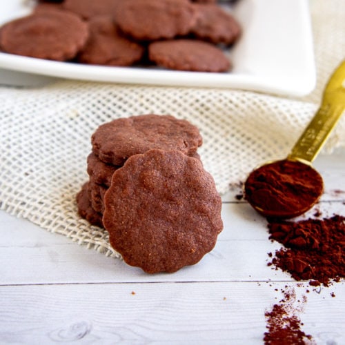 a stack of chocolate cookies next to cocoa powder