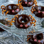 a platter of chocolate donuts decorated like spiders