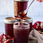 a spoon drizzling pomegranate syrup from the jar