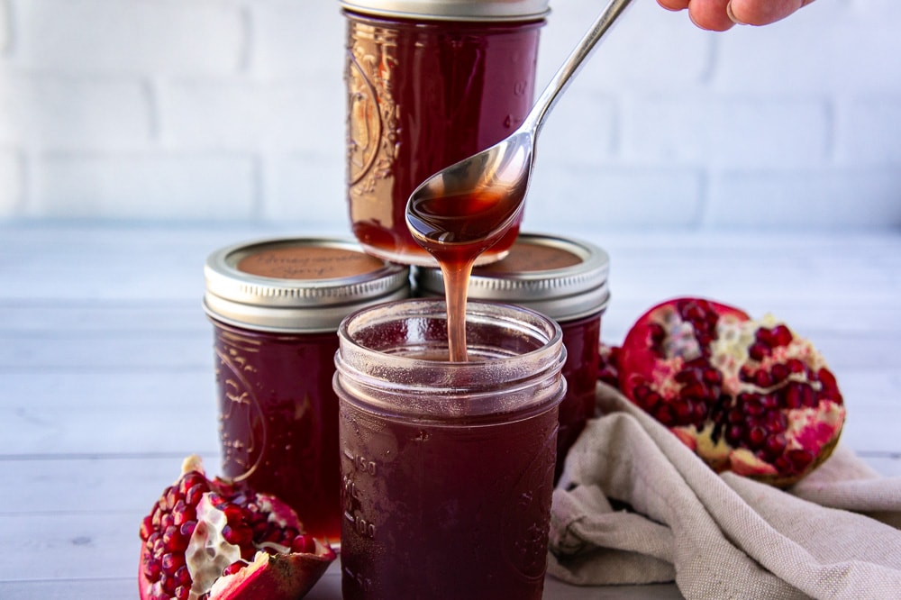 a spoon drizzling pomegranate syrup from the jar