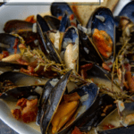 white bowl with mussels, bacon, and thyme in cider cream