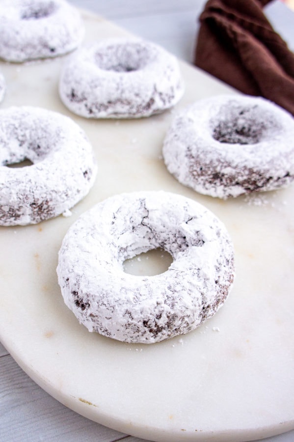 powdered sugar coated chocolate baked donuts on a white cutting board