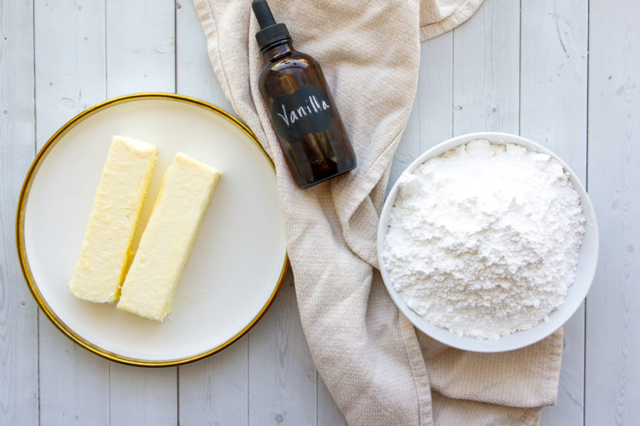 the 3 ingredients needed for vanilla buttercream, butter, powdered sugar, and vanilla on a white table