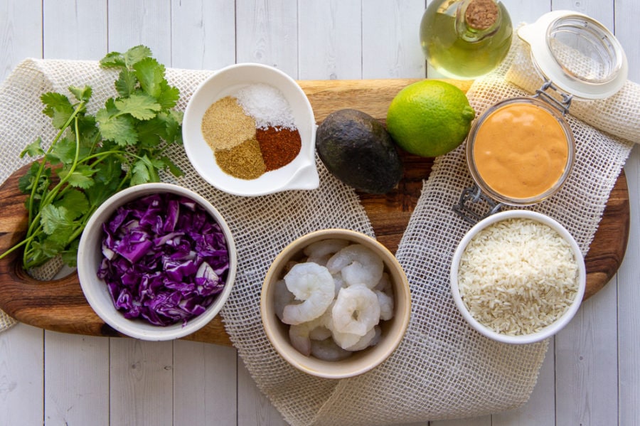 ingredients to make chipotle shrimp bowls including avocado, lime, rice, cabbage, and spice blends