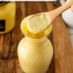 A spoon displaying creamy dijon mustard sauce in a glass jar