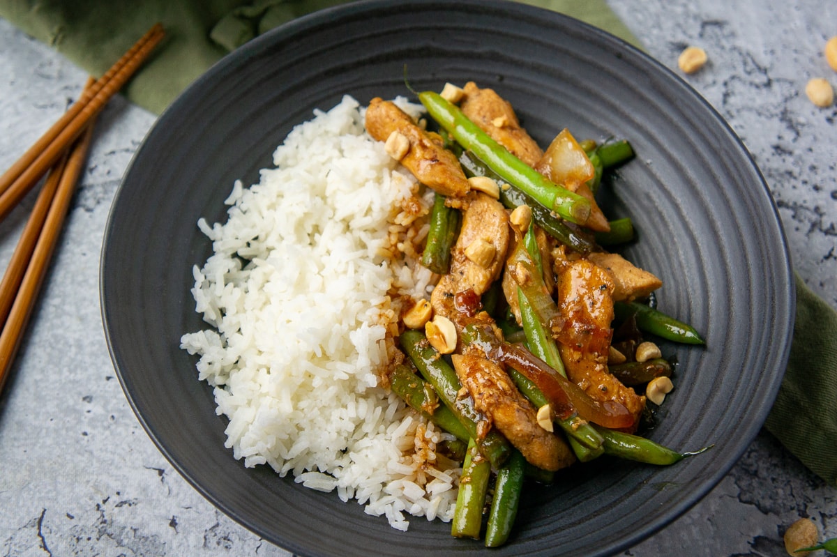 a black bowl with stir fried green beans, chicken, and rice