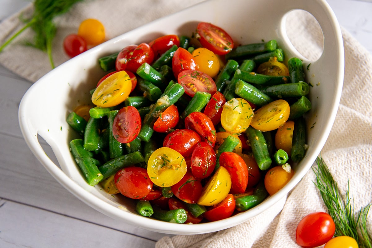a white bowl with green beans and tomatoes in dressing