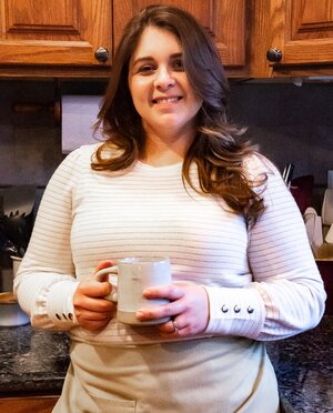 mikayla author of the flour handprint standing in a kitchen with a cup of coffee