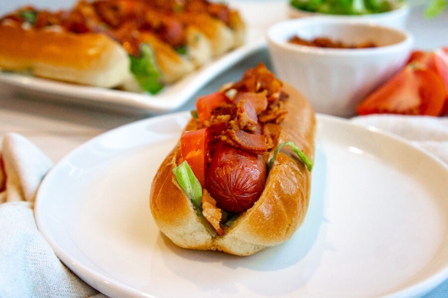 a hot dog layered with bacon, lettuce, and tomatoes on a bun