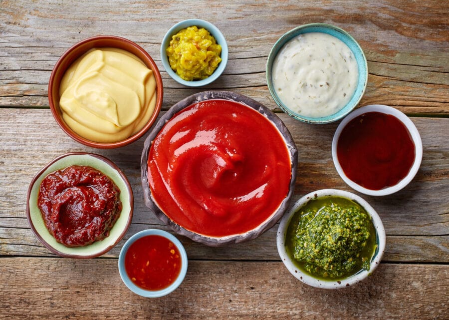 bowls of condiments and toppings used for a hot dog bar like ketchup, relish, bbq sauce, and mustards.
