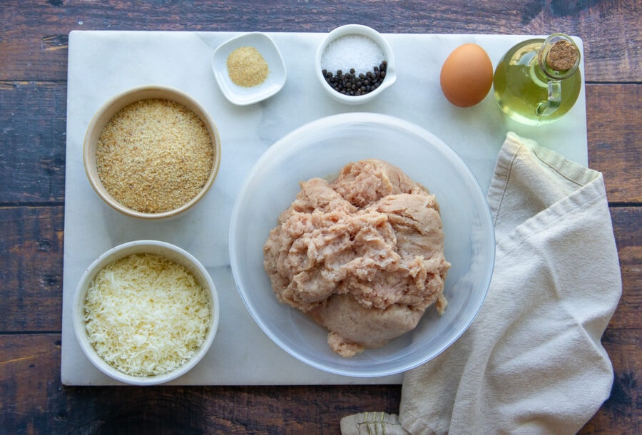 ingredients to make chicken patties including parmesan, ground chicken, breadcrumbs, and seasonings.