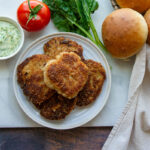 cooked homemade ground chicken patties on a plate with burger buns, tomato, and mayo.