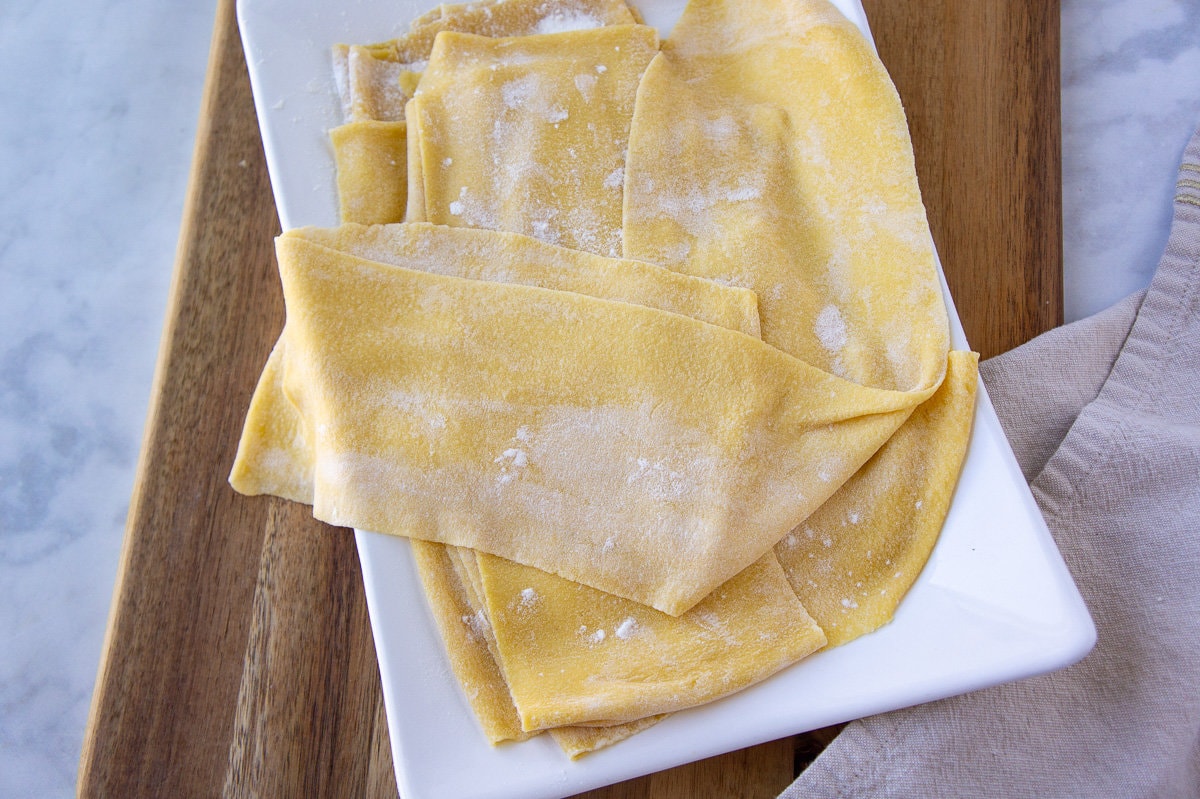 a white plate with sheets of rolled out semolina pasta dough.