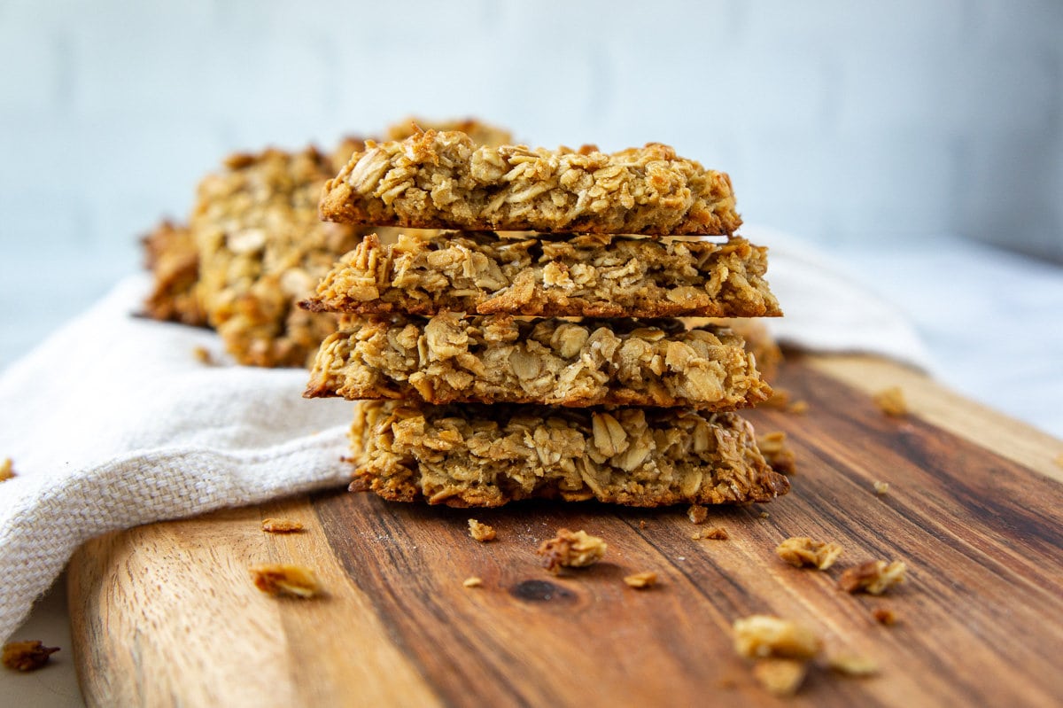 a stack of baked granola bars on a wooden cutting board.