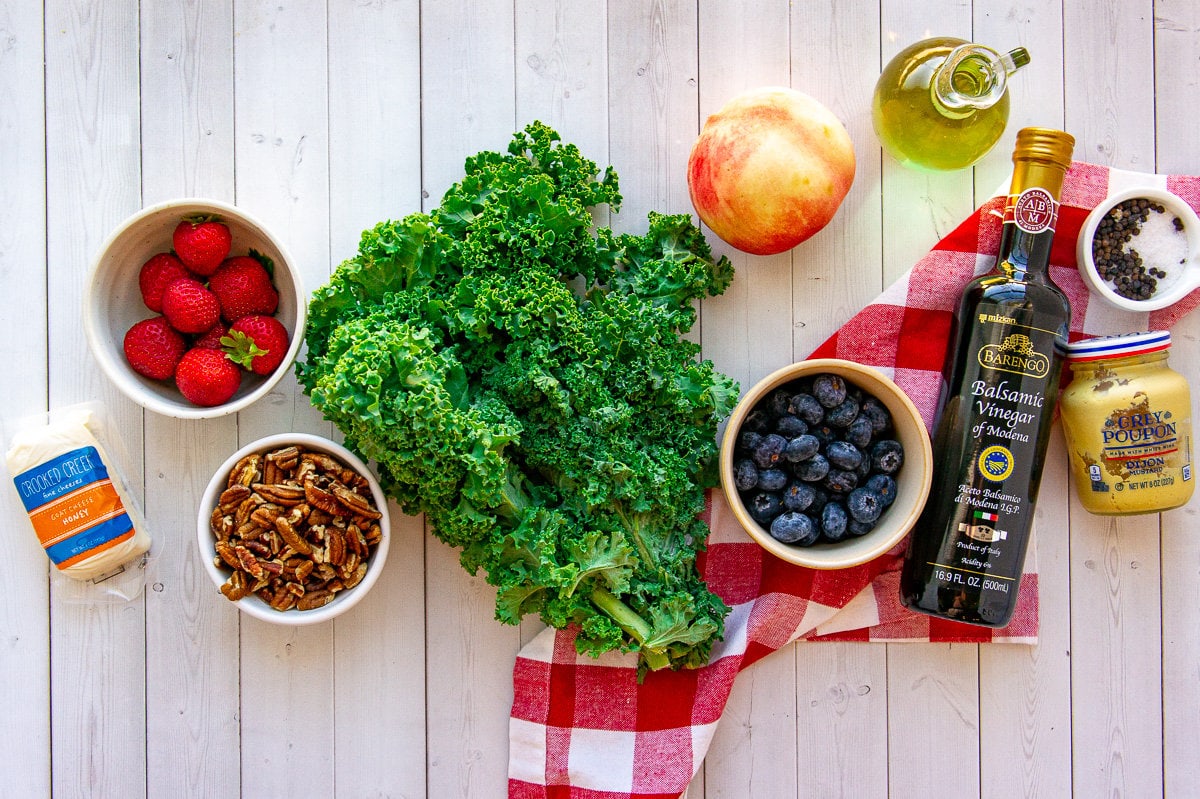 Ingredients for making a summer kale salad with blueberries, goat cheese, peaches, and pecans.