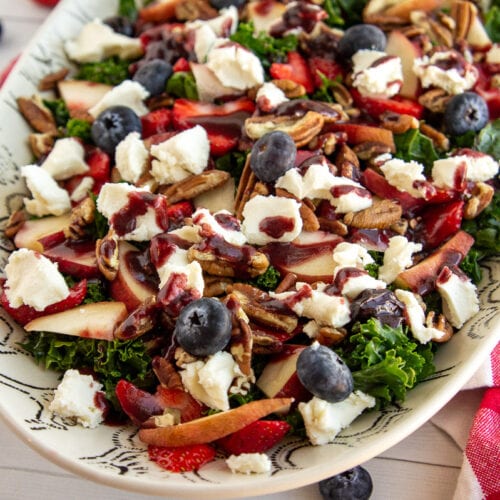 a white bowl with salad made with kale, fruit, nuts, and cheese.