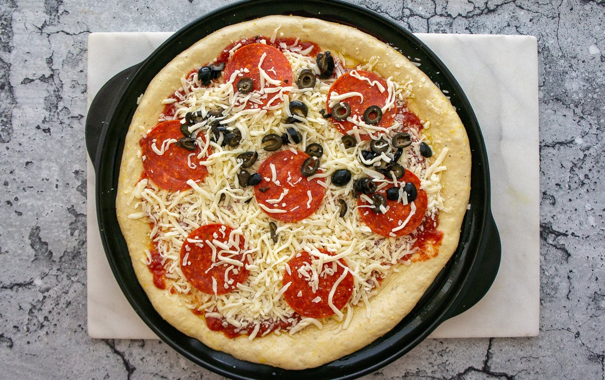 a pizza with pepperoni, cheese, and olives ready to bake.