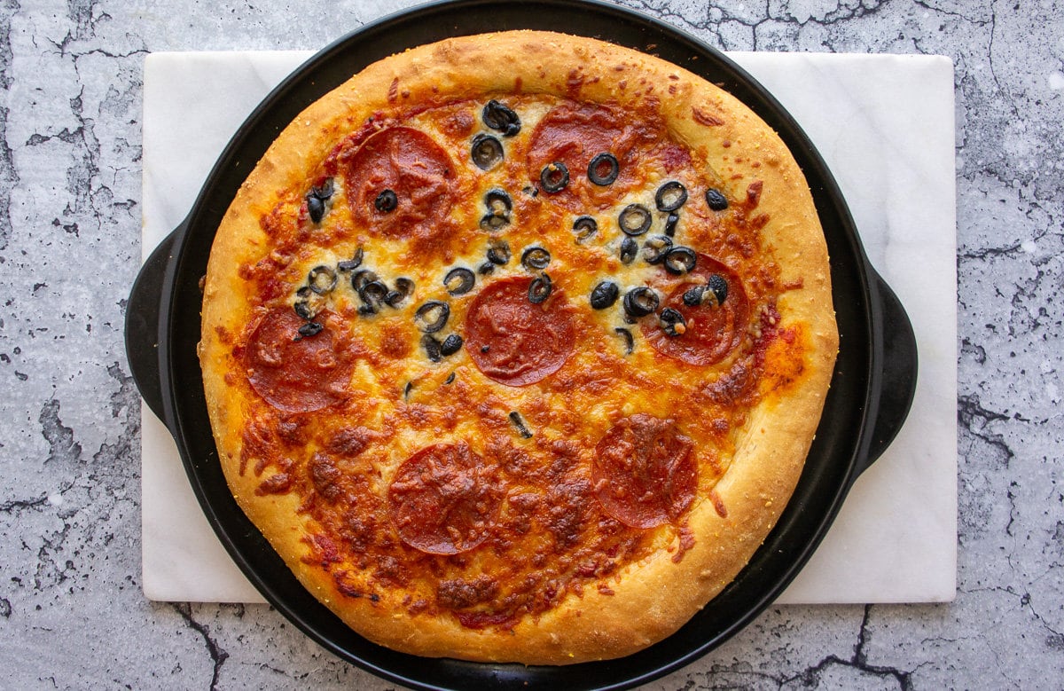 a baked pizza with olives, cheese, and pepperoni on top.