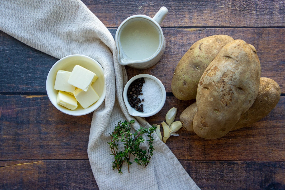 ingredients to make mashed potatoes with thyme and garlic on a wood table.